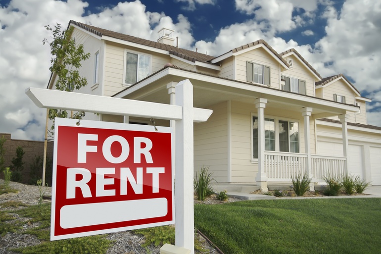 White two-story home with a front porch, barn-style windows, lush green grass, and a for rent sign in the front.