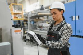 A close-up female factory worker operating machinery using a digital tablet in a modern industrial plant.