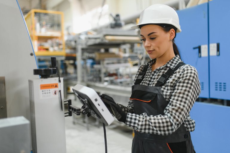 A close-up female factory worker operating machinery using a digital tablet in a modern industrial plant.