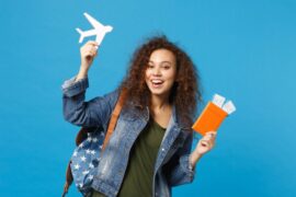 Young woman student in denim clothes, backpack, holding two plane tickets, a plane toy, and an orange passport.