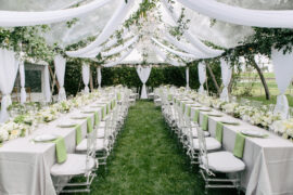 Two long tables are set up with chairs running along each side of both tables. There is a white cloth on both tables.