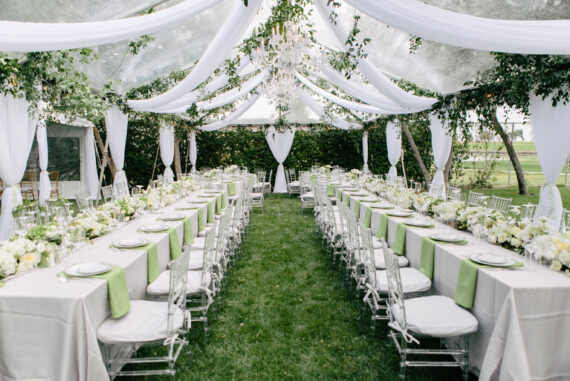Two long tables are set up with chairs running along each side of both tables. There is a white cloth on both tables.