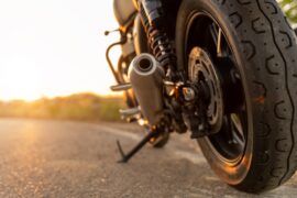 A close-up of a motorcycle's back tire sitting on the road. The kickstand is out and the sun is setting in the back.
