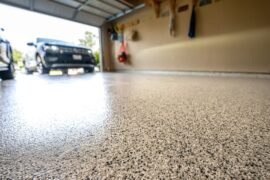 A garage floor with a fresh coating of epoxy and flakes. There are cars parked in the driveway behind the garage door.