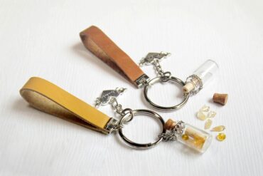Two handmade keychains with leather straps, heart-shaped charms with inscriptions, and jars of yellow stones.