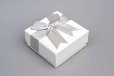 A small, white rectangular box sits on a gray background. A silky gray bow is wrapped around the white box.