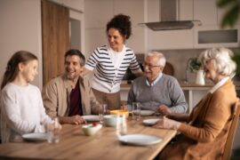 Multi-generational family gathered around a dining table, smiling and sharing a meal together in a bright, modern kitchen.