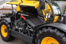 A piece of yellow heavy machinery has it’s battery hatch open. Inside the hatch is the battery and other electrical components.
