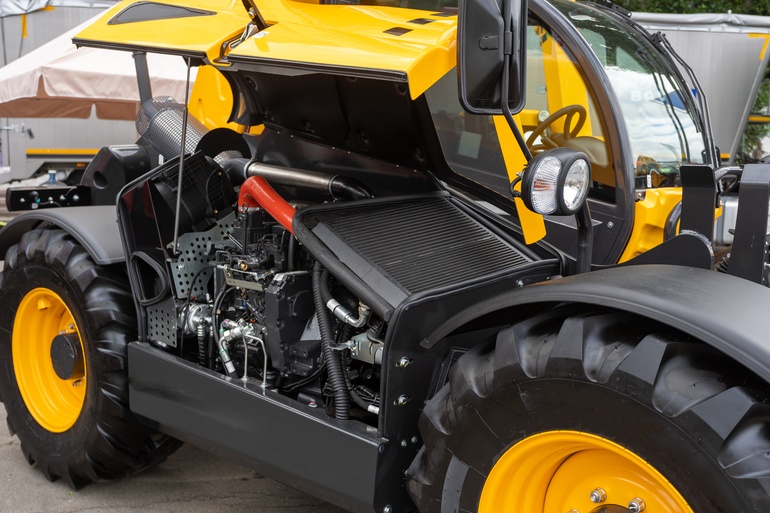A piece of yellow heavy machinery has it’s battery hatch open. Inside the hatch is the battery and other electrical components.