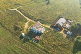 An aerial view of a rural property with two main houses or buildings. The roof on the house is not finished.