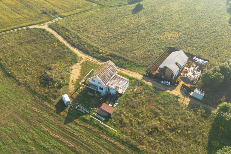 An aerial view of a rural property with two main houses or buildings. The roof on the house is not finished.