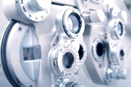 Close-up of an optometry phoropter with dials and lenses, showing detailed adjustment knobs and markings.