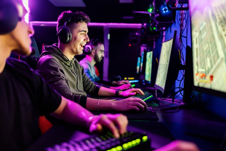 A group of esports players at a long desk with individual computers, competing under bright lights in a lively setting.