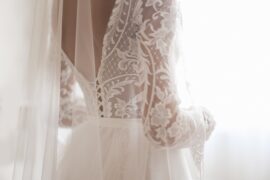 A close view of a white lace dress with sheer sleeves and fabric tied around the waist against a bright background.