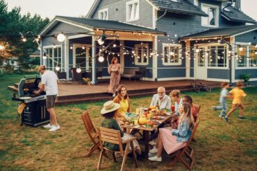 A large family with grandparents, parents, and children spending time in the home backyard around a table.