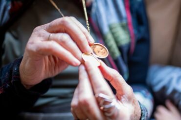 A close-up of someone's hands as they hold onto their locket necklace. The necklace features a small photo.