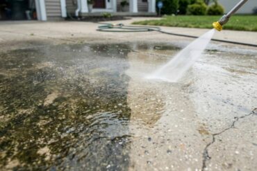 A closeup on a pressure washing nozzle on a hose that is spraying a layer of dirt off of a concrete driveway.