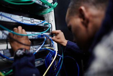A man wearing a blue sweater is using a screwdriver to tighter screws on a large network cable server.