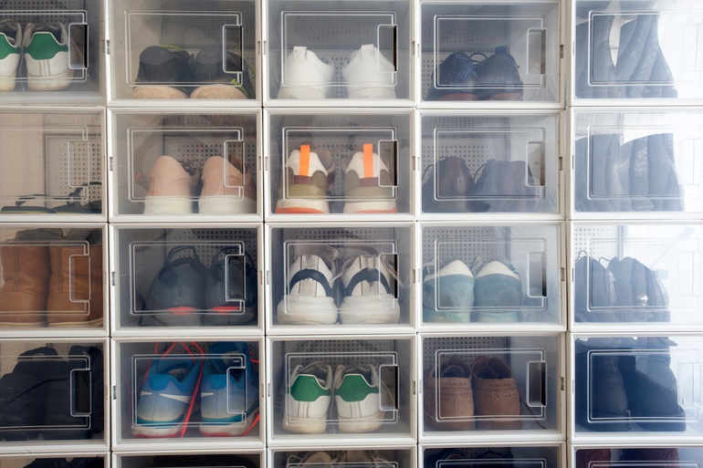 Multiple pairs of sneakers, boots, and casual shoes neatly arranged in stacked transparent plastic storage boxes.