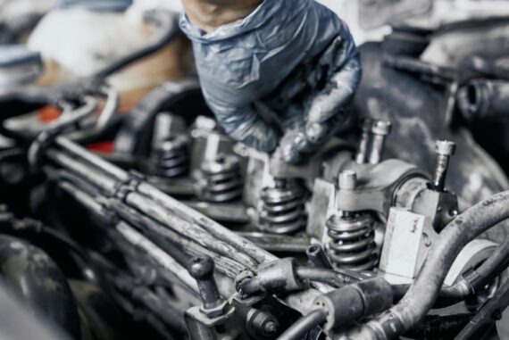 A person wearing a protective glove is working on a vehicle’s engine. There are many tubes and mechanical parts.