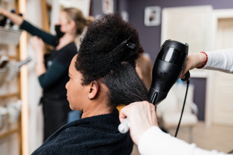 Hairstylist blow-dries and brushes a client’s natural hair during a salon appointment.